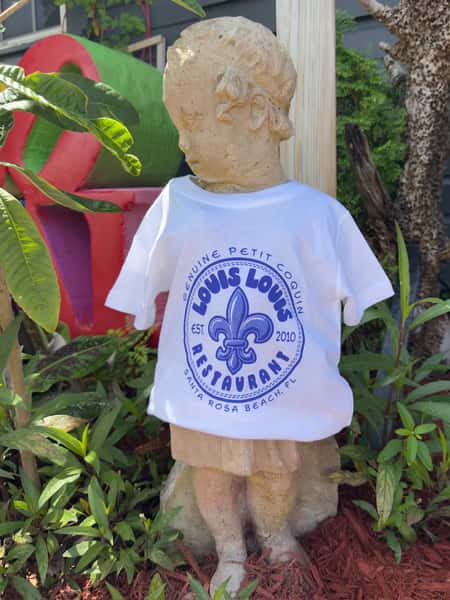A stone statue of a child wearing a white T-shirt with the "LOUIS LOUIS Restaurant" logo, featuring a fleur-de-lis and "Santa Rosa Beach, FL."