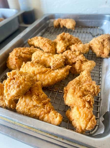 Golden fried chicken tenders resting on a wire rack, featuring crispy breading and classic comfort food appeal in a casual Southern kitchen setting.