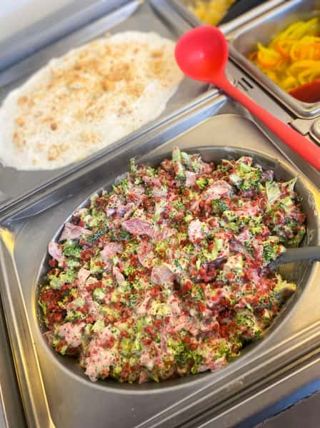 Creamy broccoli salad with diced ham, red onion, shredded cheddar, and bacon bits on a Southern buffet line, served alongside classic homestyle sides.