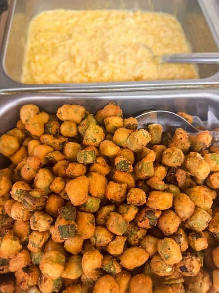 Crispy fried okra bites on a hot buffet line with creamy mac and cheese in the background, highlighting classic Southern sides in a homestyle restaurant setting.