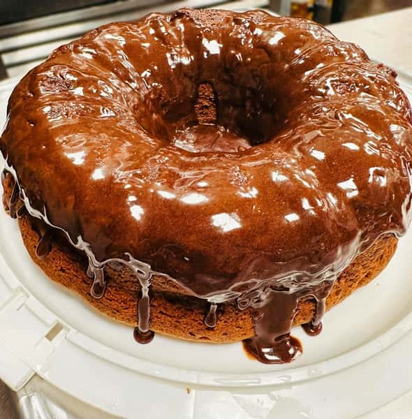 Chocolate-glazed bundt cake with rich ganache dripping over the sides, presented as a decadent Southern dessert in a bakery or restaurant display.