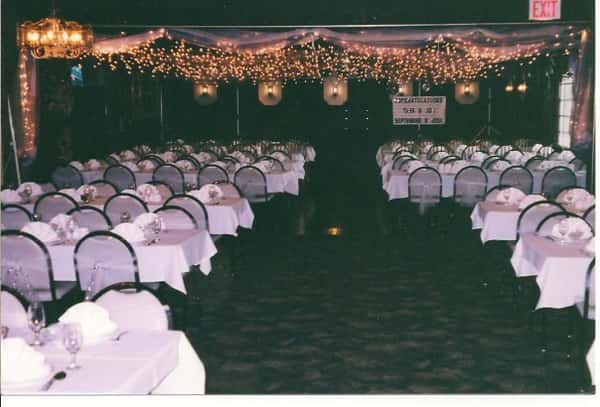 Room with long rectangular tables and chairs - the tables have plates, utensils and coffee mugs set up with roses as centerpieces