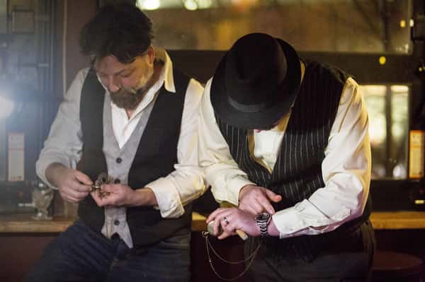 two men dressed in 1920s era checking their watches