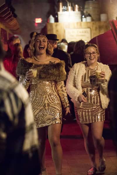 Two ladies in flapper outfits coming into the event with drinks in their hand