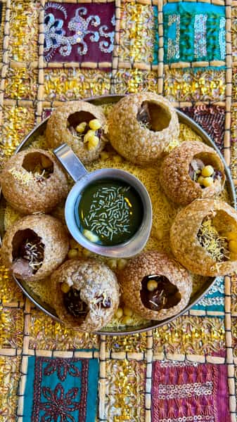 A plate of crispy pani puri filled with chickpeas and tamarind, served with a bowl of green chutney, surrounded by crunchy sev.