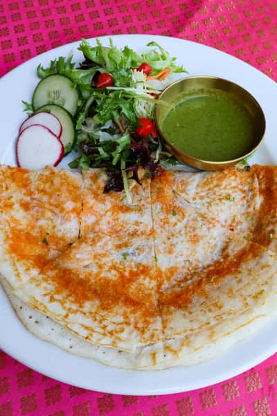 A crispy dosa served with a fresh salad and a bowl of green chutney.
