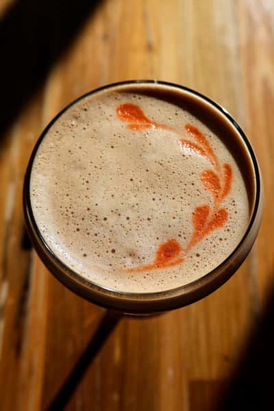 A close-up of a beautifully crafted espresso martini, topped with creamy foam and a delicate swirl of red garnish.