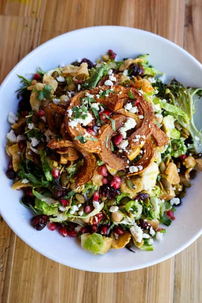 A vibrant salad with fresh greens, roasted pumpkin slices, pomegranate seeds, and a variety of toppings, creating a colorful and healthy dish.