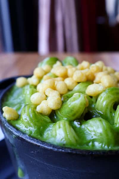 A close-up of green pasta with a creamy sauce, topped with crispy fried pieces, served in a cast iron skillet.