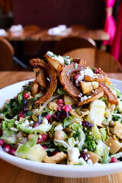 A vibrant salad with fresh greens, roasted pumpkin slices, pomegranate seeds, and a variety of toppings, creating a colorful and healthy dish.