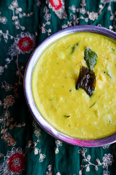 A bowl of yellow lentil soup, garnished with bay leaves, on a floral embroidered cloth.