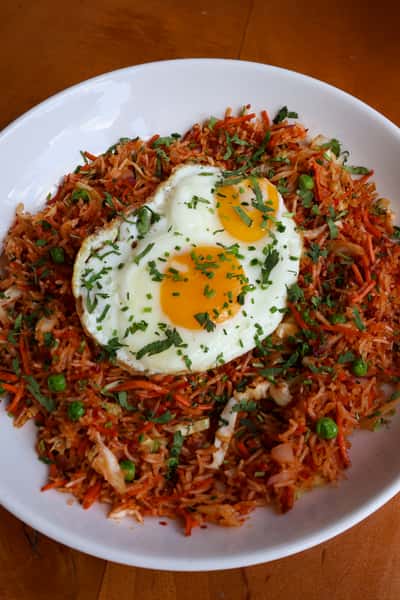 A plate of fried rice with vegetables and two sunny-side-up eggs, topped with chopped cilantro.