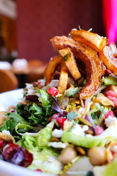 A vibrant salad with fresh greens, roasted pumpkin slices, pomegranate seeds, and a variety of toppings, creating a colorful and healthy dish.