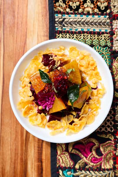 A colorful salad featuring roasted pumpkin and beetroot, garnished with fresh herbs, edible flowers, and vibrant fruit pearls.