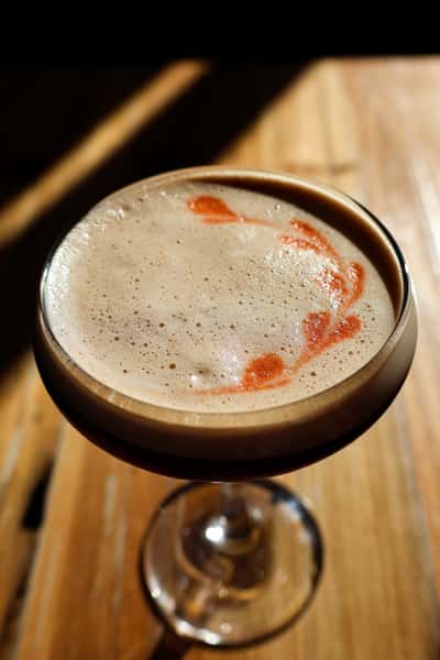A close-up of a beautifully crafted espresso martini, topped with creamy foam and a delicate swirl of red garnish.