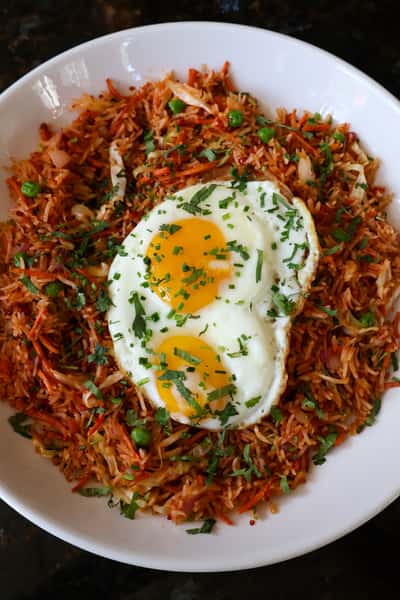 A plate of fried rice with vegetables and two sunny-side-up eggs, topped with chopped cilantro.