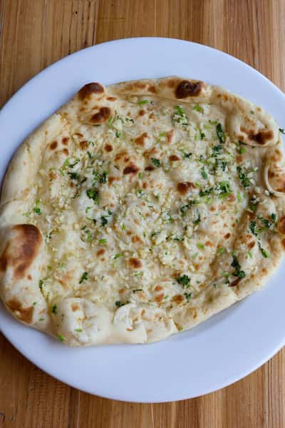 A freshly baked garlic naan garnished with chopped cilantro, showcasing golden-brown edges and soft texture.