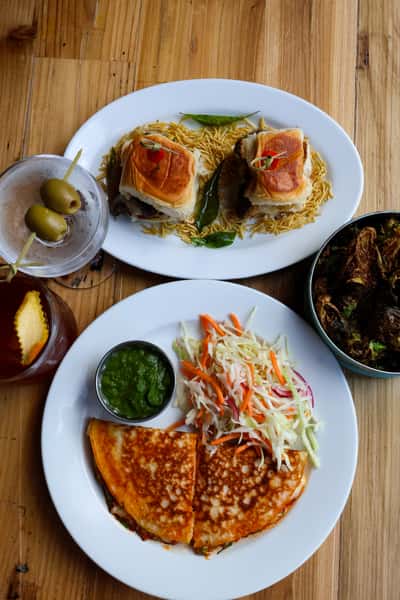 Two plates with flavorful dishes: one featuring slider sandwiches with crispy fries, and the other showcasing a quesadilla, green chutney, and a side salad.