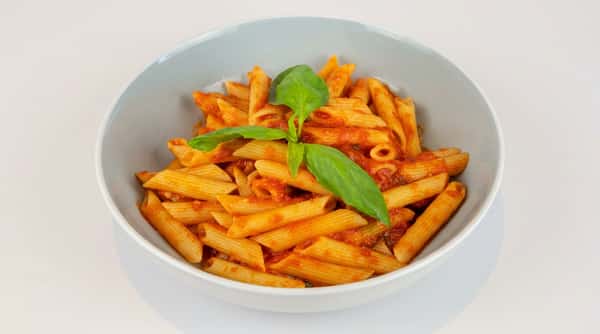 Penne pasta with red tomato sauce in a grey bowl, garnished with a sprig of fresh basil.