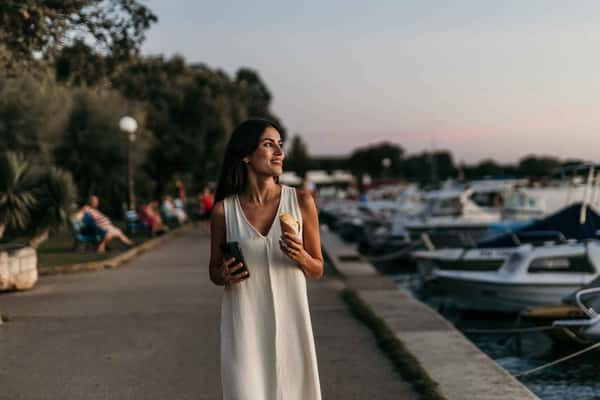 woman walking by the docks while holding an ice cream
