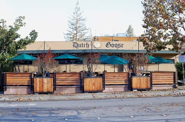 Exterior view of Dutch Goose restaurant with patio seating under green umbrellas and planters lining the sidewalk — a welcoming neighborhood spot for outdoor dining.