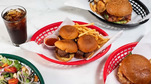 Trio of mini beef sliders served with fries and ketchup, accompanied by a fizzy cola and classic burgers — casual American comfort food in a vibrant diner setting.