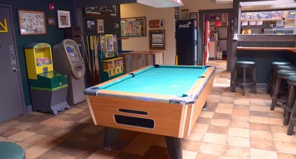Game room inside Dutch Goose with a pool table, arcade machines, and bar seating, offering a relaxed and entertaining hangout space.