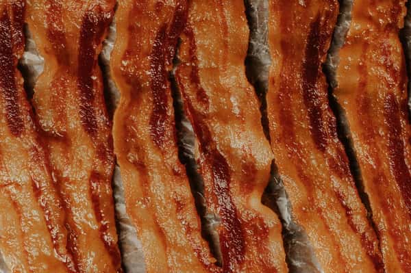 Close-up of crispy oven-cooked bacon strips with rich, smoky glaze and sizzling texture – classic breakfast meat perfect for brunch menus or burger and pizza toppings.