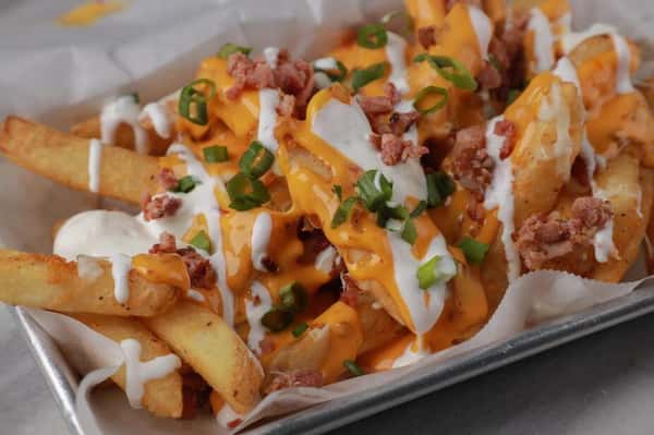 Loaded French fries topped with melted cheddar cheese, crispy bacon bits, sour cream drizzle, and green onions at a sports bar and grill.