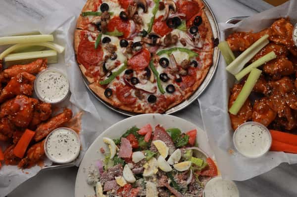 Supreme pizza topped with pepperoni, Italian sausage, black olives, mushrooms, and green bell peppers, served with buffalo wings, celery sticks, ranch dressing, and a fresh house salad – classic American pizzeria feast.