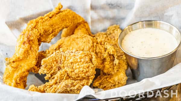 Golden fried chicken tenders served in a basket with creamy dipping sauce at a casual bar and grill.