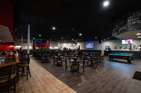 Wide view of a modern sports bar dining area featuring pool tables, multiple TVs, high-top tables, and a relaxed neighborhood pub atmosphere.
