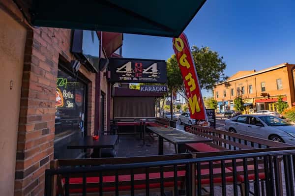 Outdoor patio dining area at a local pizza and karaoke bar, featuring fenced seating, street views, and casual neighborhood vibe.