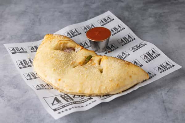 Golden-brown baked calzone filled with melted cheese and savory pizza toppings, served on branded parchment paper with a side of marinara dipping sauce – classic Italian pizzeria favorite perfect for a casual restaurant menu.
