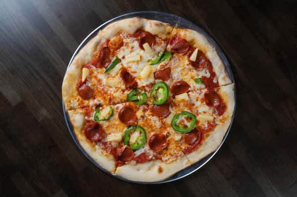 Hawaiian-style pepperoni pizza topped with melted mozzarella, sweet pineapple chunks, and fresh jalapeño slices on a hand-tossed crust – bold sweet and spicy specialty pizza from a casual pizzeria.
