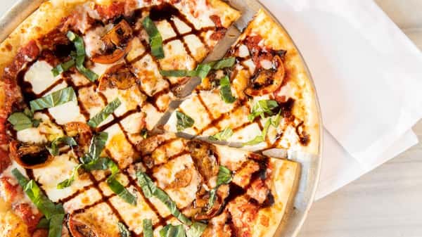 Artisan pizza topped with fresh basil, sliced tomatoes, melted mozzarella, and balsamic glaze on a thin crust at a modern pizza restaurant.
