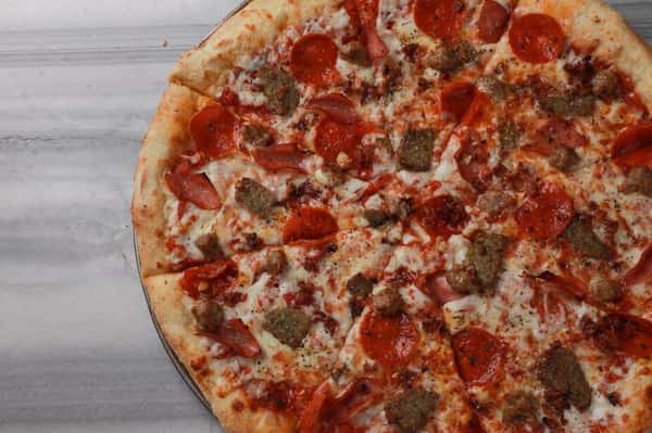 Large meat lovers pizza topped with pepperoni, sausage, and melted mozzarella on a golden crust at a neighborhood pizzeria.