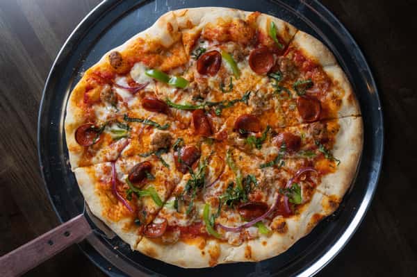 Hand-tossed supreme pizza topped with pepperoni, sausage, green peppers, red onions, and fresh basil on a metal serving tray.