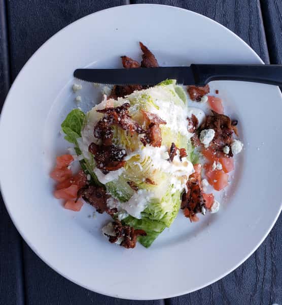 Alt text: Fresh Caesar salad topped with crispy bacon, grated Parmesan, diced tomatoes, and creamy dressing, served on a white plate at a casual sports bar.