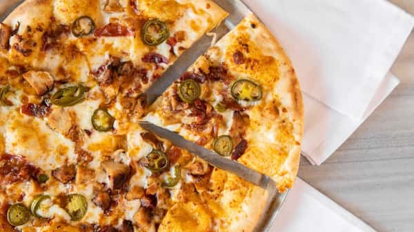 Close-up of specialty pizza topped with jalapeños, grilled chicken, bacon, and melted cheese on a crispy crust at a casual pizza restaurant.
