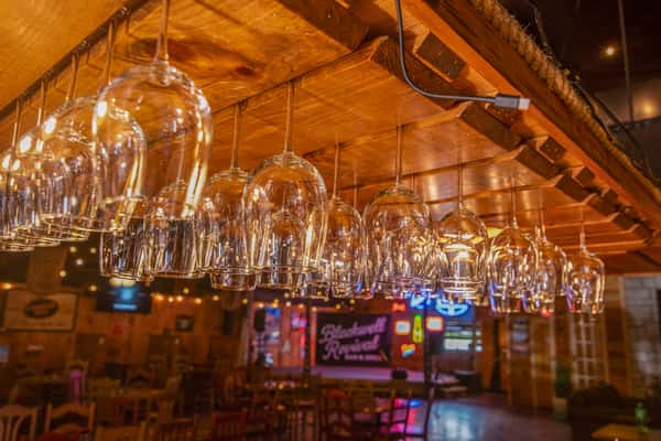 Hanging glassware above the bar at Blackwell Revival in Atkins, Arkansas, showcasing a warm rustic bar atmosphere