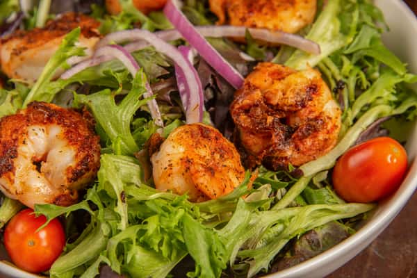 Close-up of mixed greens salad topped with grilled Cajun shrimp and fresh vegetables at Blackwell Revival in Atkins, Arkansas