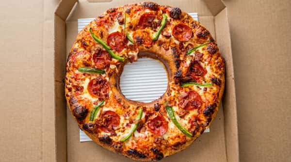 Ring-shaped pizza with pepperoni, green bell peppers, and bacon bits, in a cardboard box.