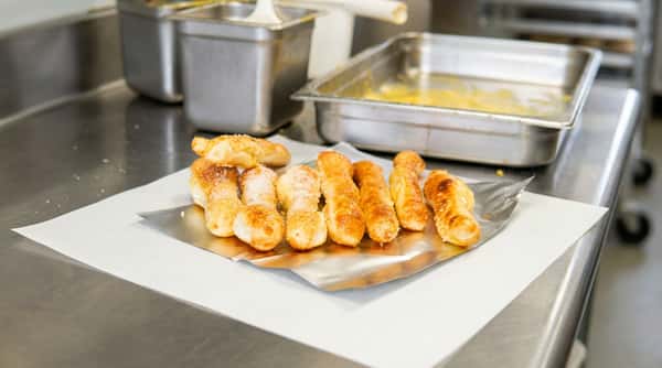 Golden-brown breadsticks, some with sugar or cheese, on foil and parchment paper, with ingredients in metal containers in the background.