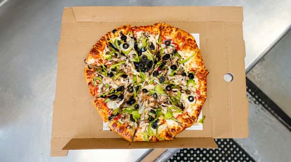 Whole pizza with green peppers, black olives, onions, and mushrooms in a cardboard box, being cut by a hand.