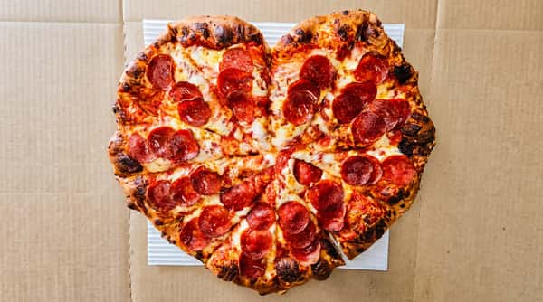 Heart-shaped pepperoni pizza with melted cheese and a well-baked crust in a cardboard box.
