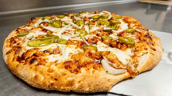 BBQ chicken pizza with melted cheese, white onions, and sliced jalapeños on a metal surface.