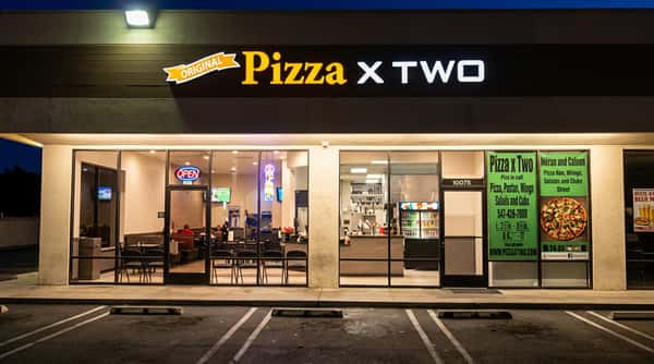 Exterior of "The Original Pizza x Two" restaurant at night, with a brightly lit storefront and glass windows.