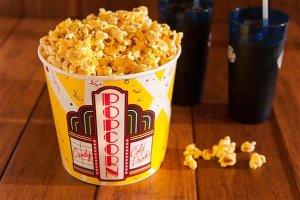 big tub of popcorn on a table next to two cokes