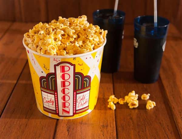 big tub of popcorn on a table next to two cokes
